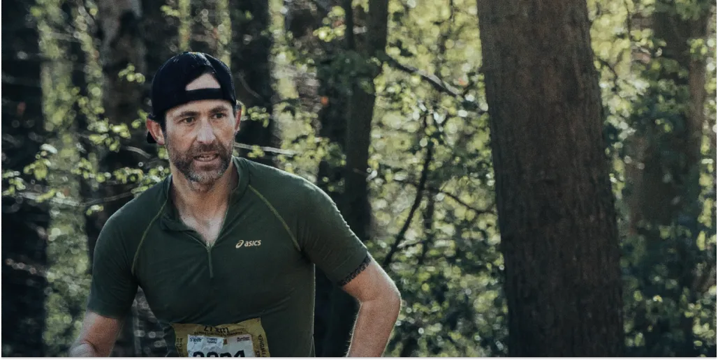 low carb athlete running in a forest wearing a green shirt and black cap.